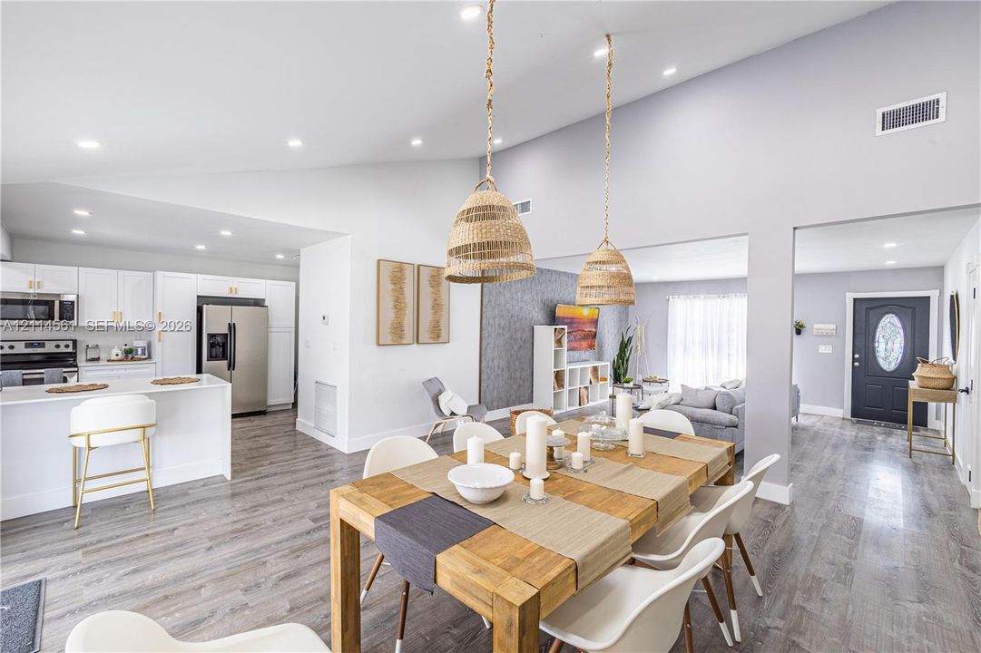 Vaulted ceilings, open-concept kitchen with white cabinetry and stainless steel appliances, wood-finish flooring, and natural-textured pendant lighting