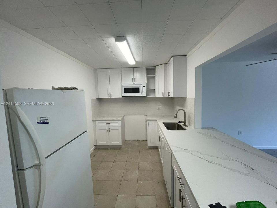 Kitchen featuring white cabinetry, stone-finish countertops, an integrated microwave, a stainless steel sink with a gooseneck faucet, and tiled flooring