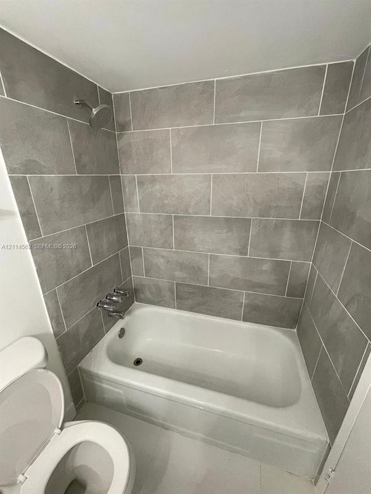 Full-height grey tile tub surround, white porcelain bathtub, chrome wall-mounted shower head, and chrome faucet hardware