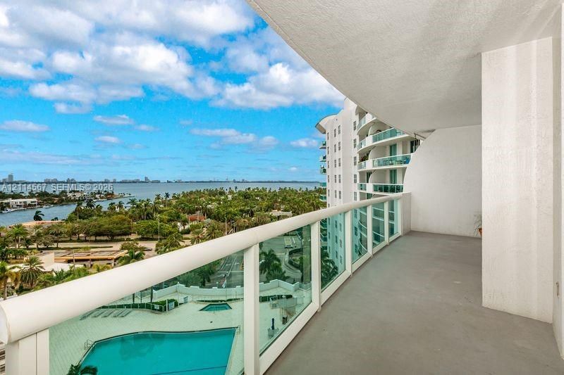 Covered balcony featuring a glass panel railing, concrete flooring, and water scenery
