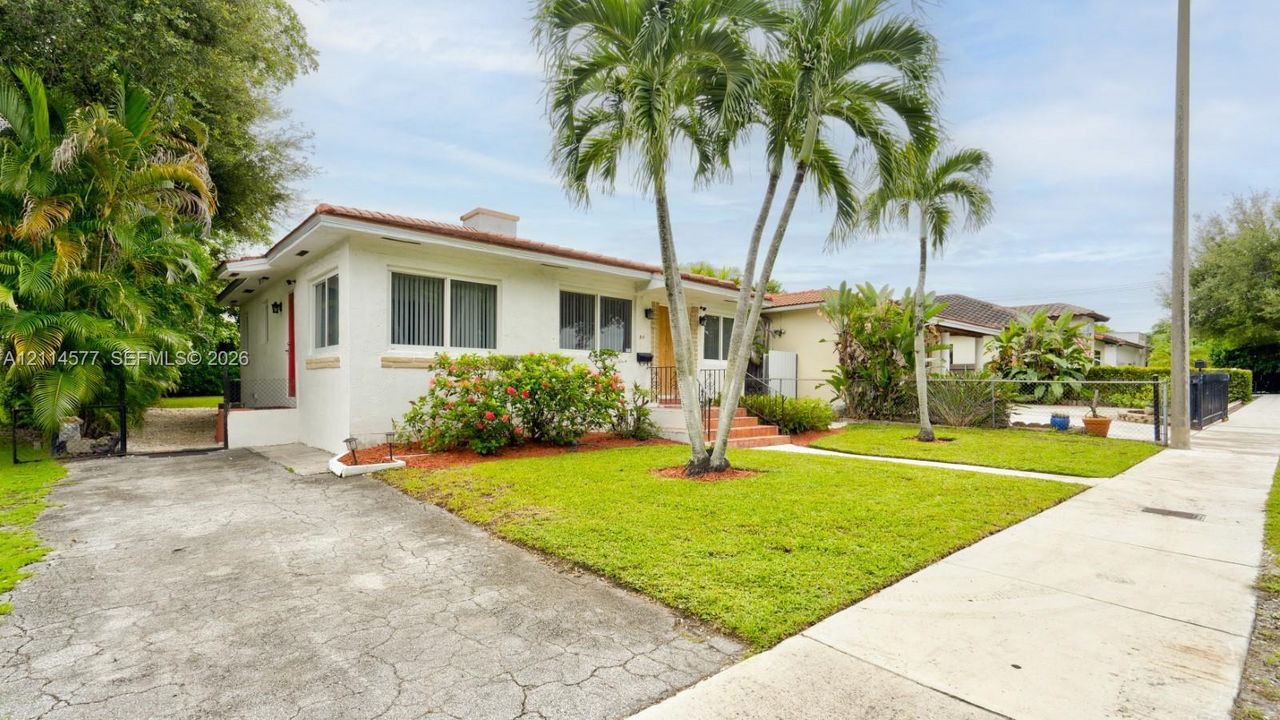 Stucco exterior residence featuring a tiled roof, concrete driveway, mature palm trees, and manicured landscaping