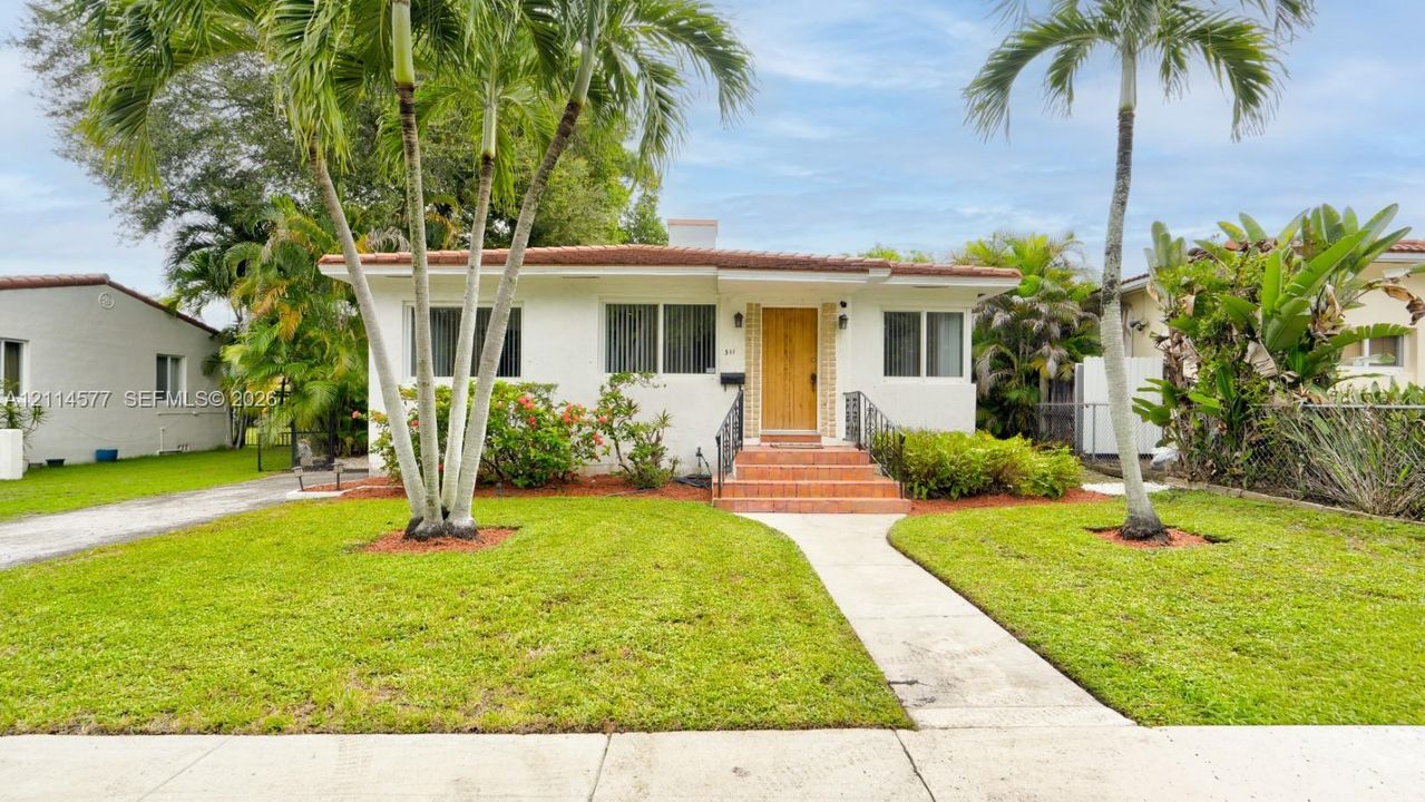 Stucco exterior with a tile roof, natural wood-finish front door, terracotta tiled entry steps, wrought iron handrails, and mature palm landscaping