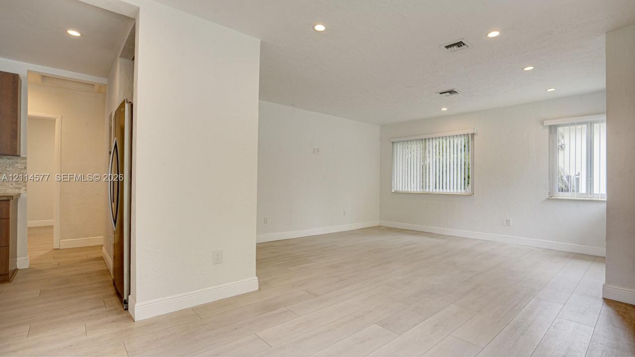 Open living area featuring wood-finish flooring, recessed lighting, and windows with vertical blinds