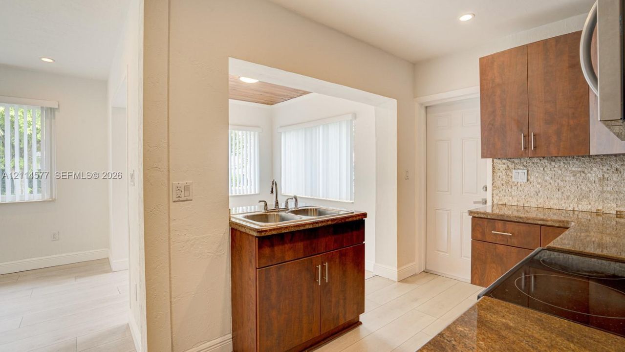 Kitchen featuring wood-finish cabinetry, stone-texture countertops, a dual-basin stainless steel sink, tiled backsplash, and light-toned wood-finish flooring