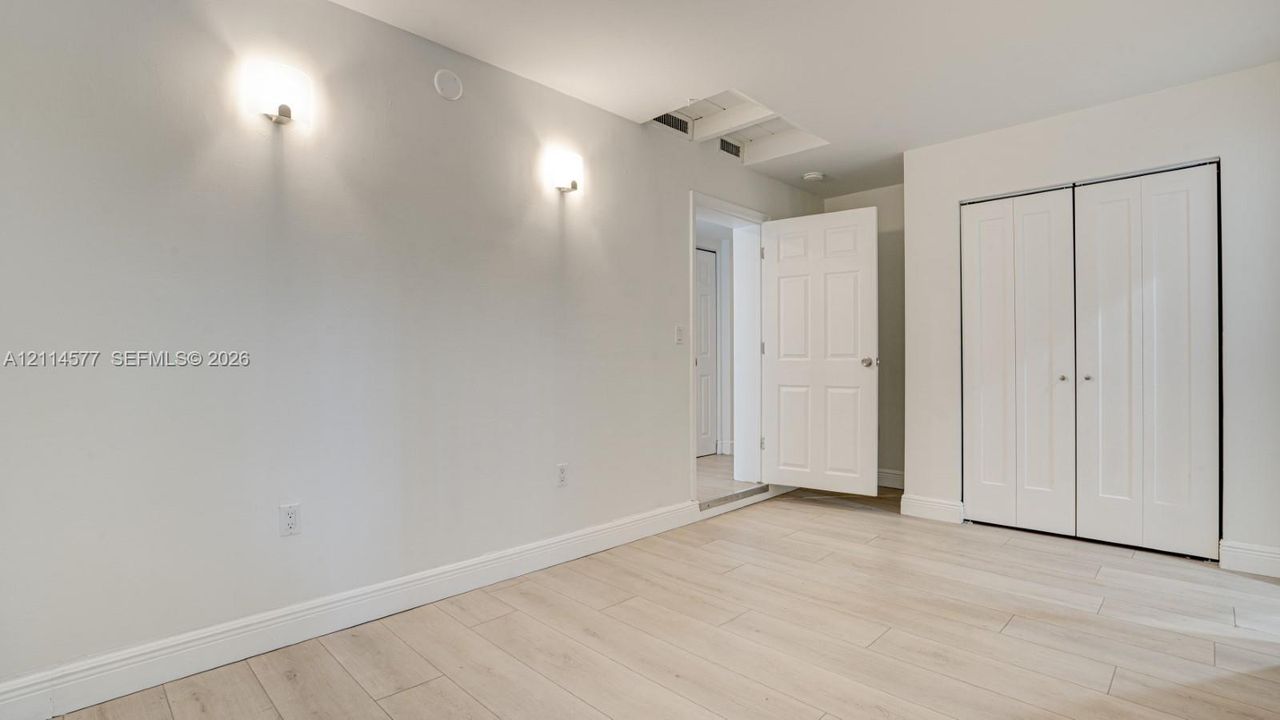 Interior space featuring light-toned wood-finish flooring, neutral walls, two wall-mounted light fixtures, and a white six-panel closet door
