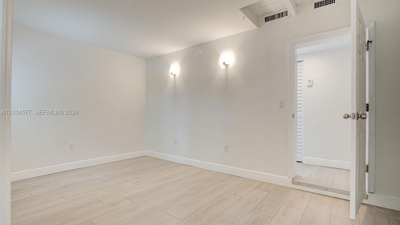 Neutral interior space featuring wood-finish flooring, dual wall-mounted light fixtures, and a six-panel interior door