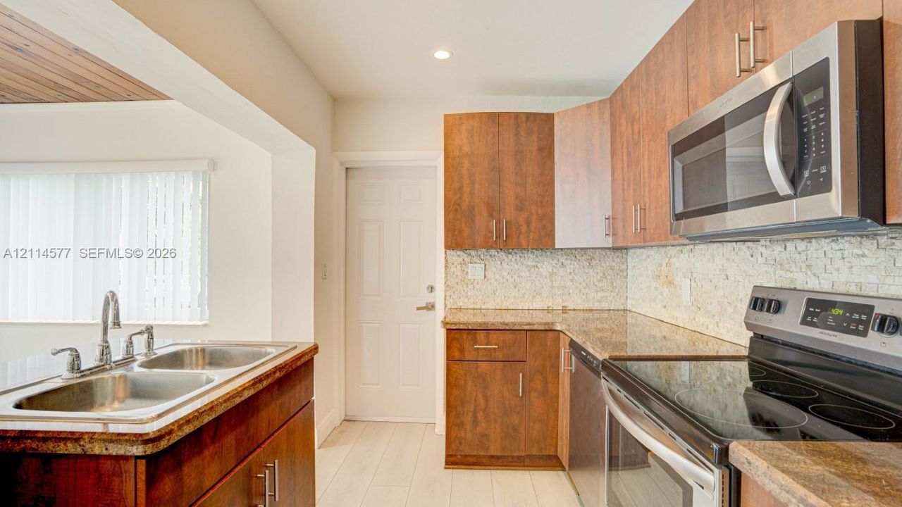 Kitchen featuring wood-finish cabinetry, stone-texture countertops, a mosaic tile backsplash, and stainless steel appliances