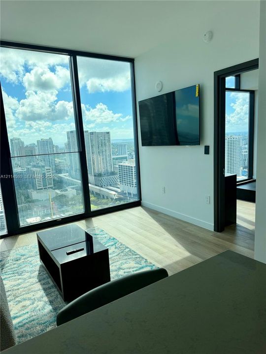 Floor-to-ceiling windows with urban skyline scenery, wood-finish flooring, and black door frames