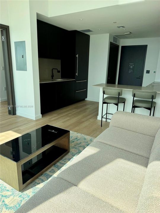 Kitchenette featuring sleek matte black cabinetry, a built-in refrigerator, neutral-toned countertops, and a matte black faucet, complemented by light-toned wood-finish flooring