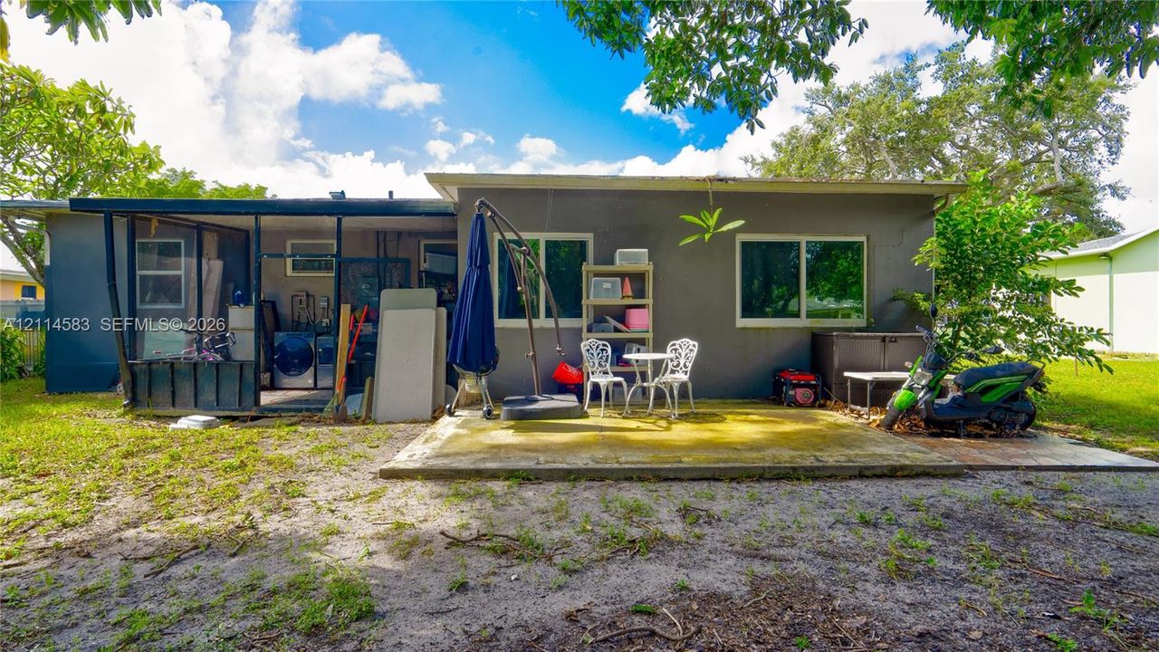 Rear exterior featuring a concrete patio, a screened enclosure, and mature trees