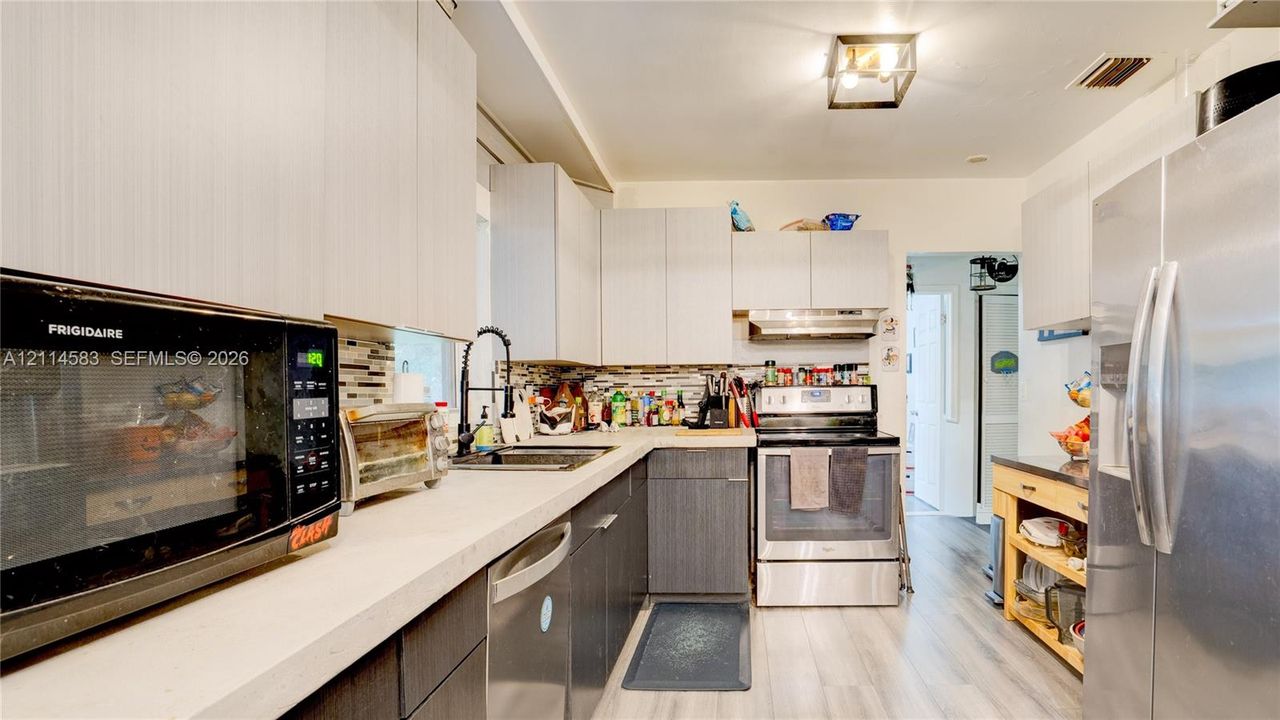 Kitchen featuring flat-panel cabinetry, light-toned countertops, multi-material tile backsplash, stainless steel appliances, and wood-finish flooring