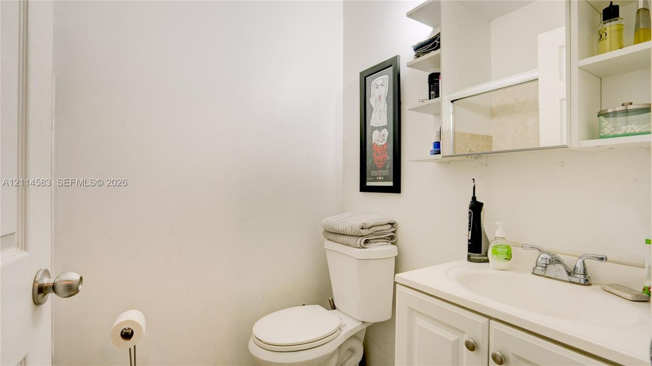White vanity cabinet featuring an integrated sink, polished chrome dual-handle faucet, and overhead cabinetry with built-in shelving and mirror