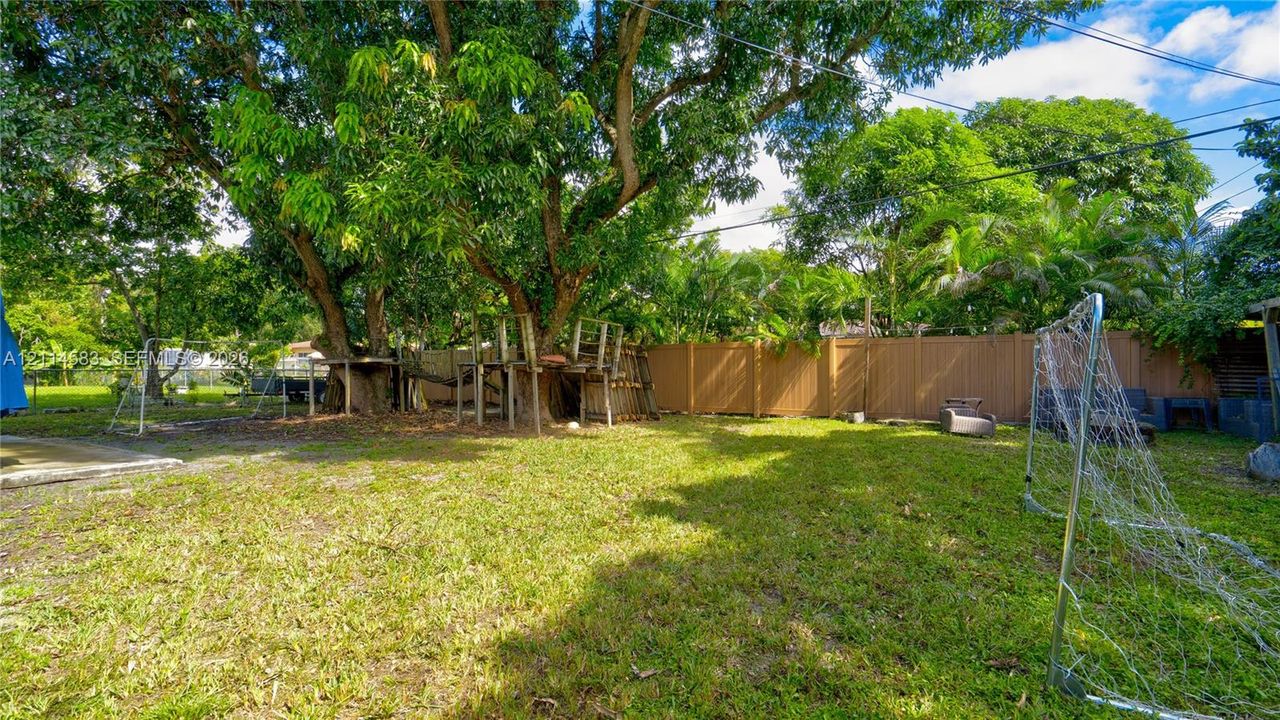Expansive backyard featuring mature tree canopy, integrated wooden platform structure, and solid perimeter fencing