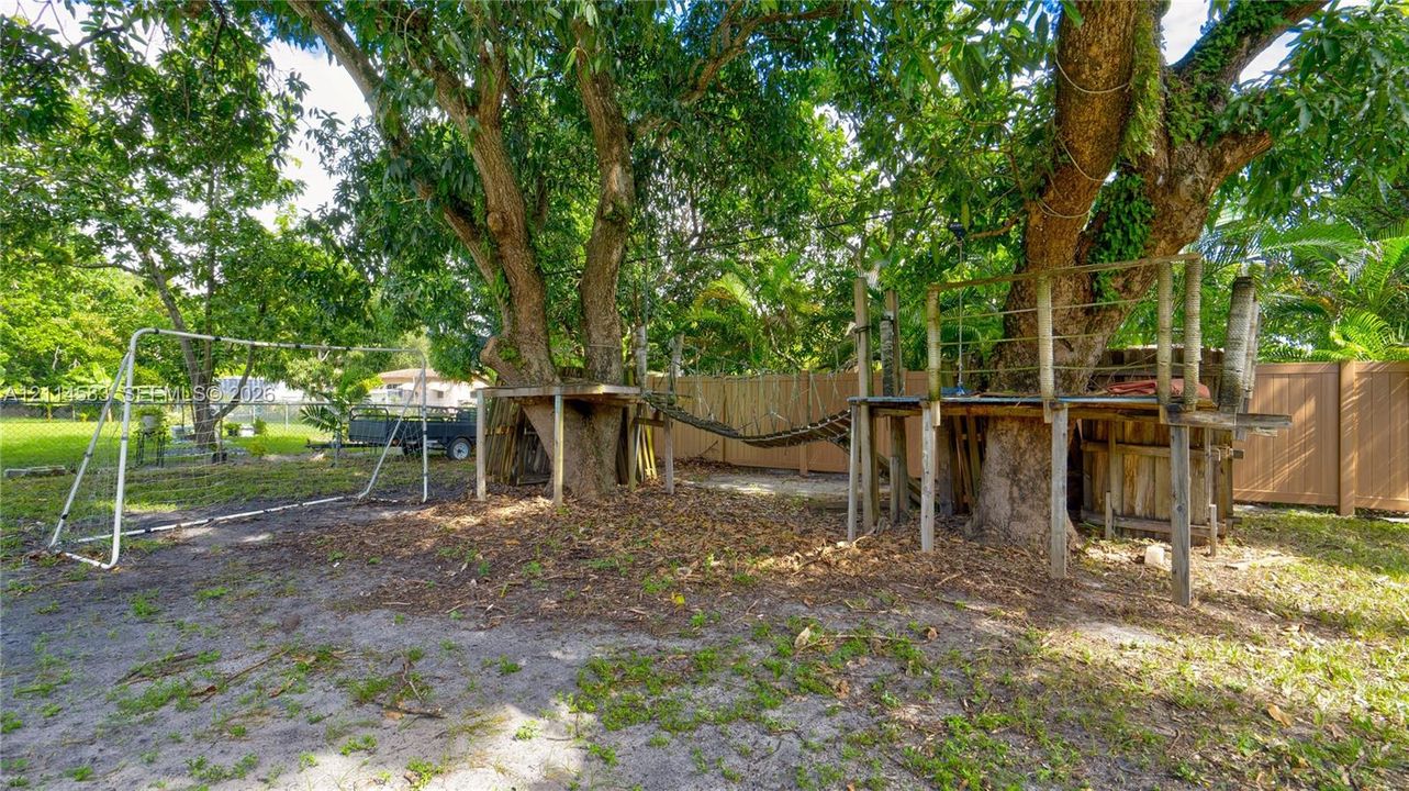 Spacious backyard featuring mature trees, a built-in wooden elevated platform structure, and perimeter fencing
