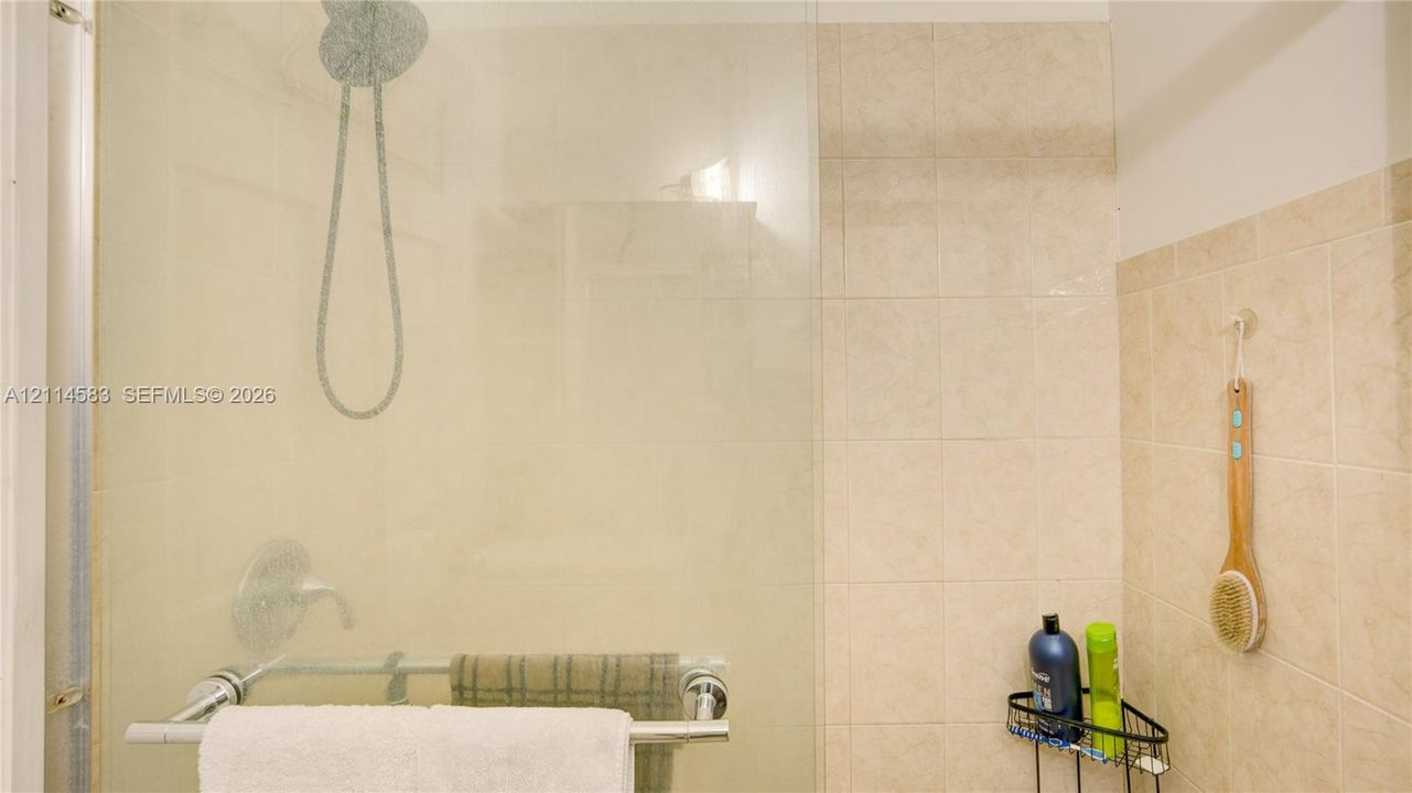 Walk-in shower featuring a frameless glass enclosure, polished chrome rainfall showerhead, wall-mounted control valve, and neutral tile wall surround