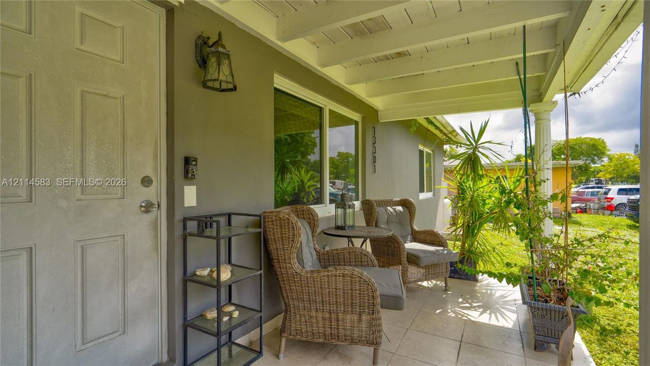 Covered front porch featuring tile flooring, exposed beam ceiling, decorative column, and wall-mounted exterior lighting