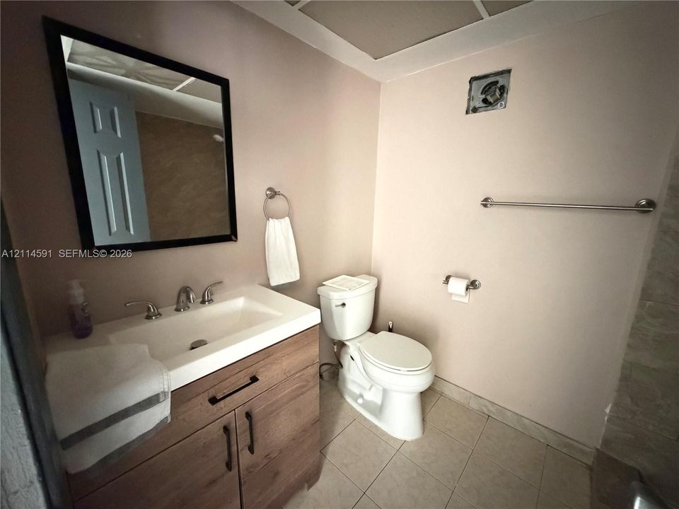 Wood-finish vanity cabinet, white porcelain sink, rectangular wall mirror with a dark frame, and neutral tile flooring