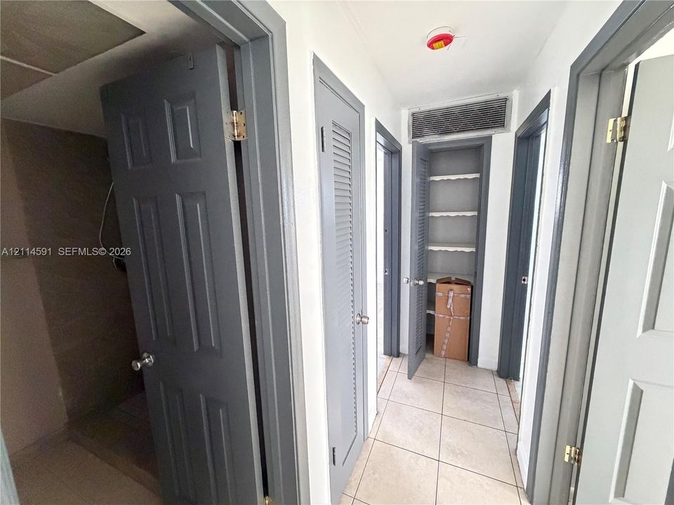 Hallway featuring large-format ceramic tile flooring, neutral wall paint, and multiple gray-painted interior doors