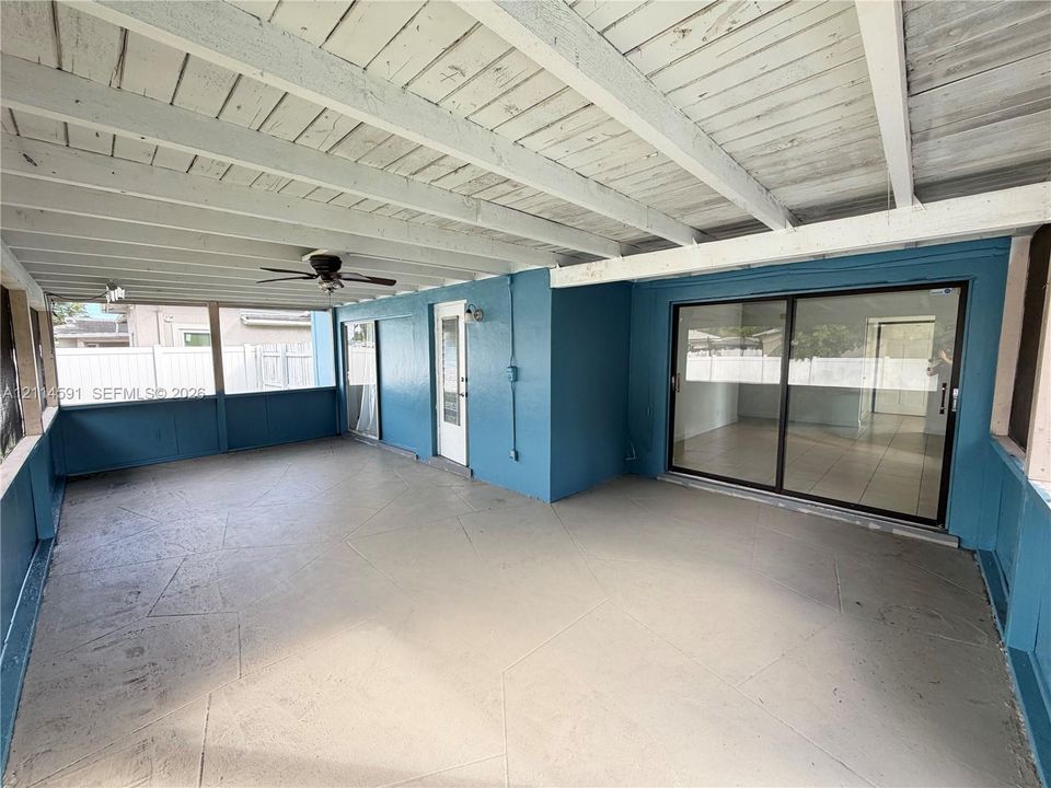 Covered patio featuring an exposed beam ceiling, a ceiling fan, a concrete floor with scored geometric detailing, and sliding glass doors