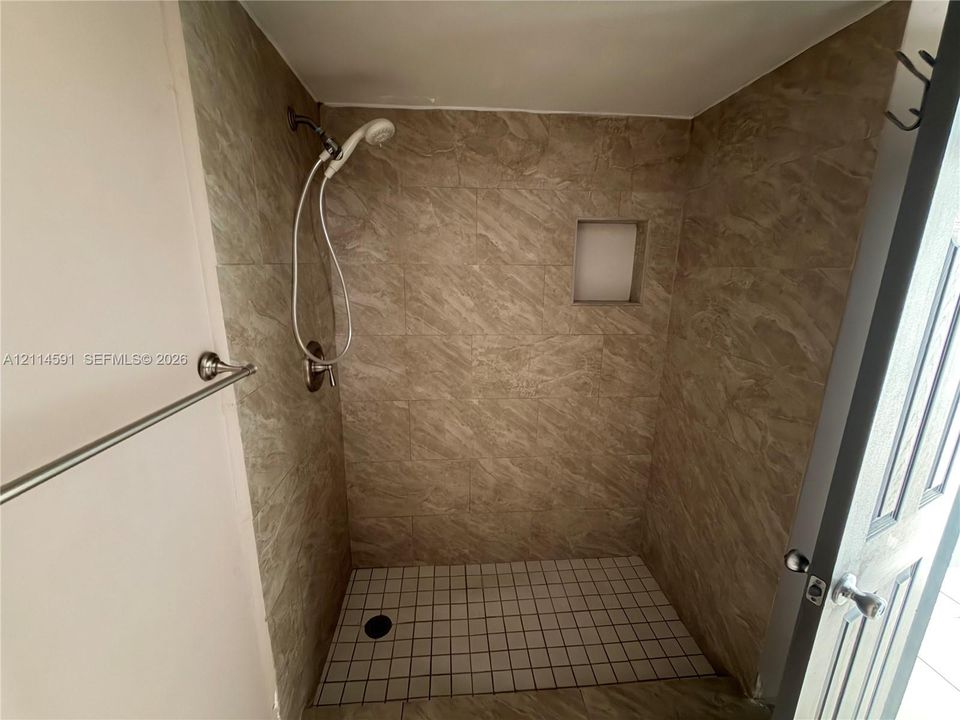 Walk-in shower featuring neutral stone-finish wall tile, a built-in recessed wall niche, a square-tile shower floor, and a polished chrome handheld shower fixture