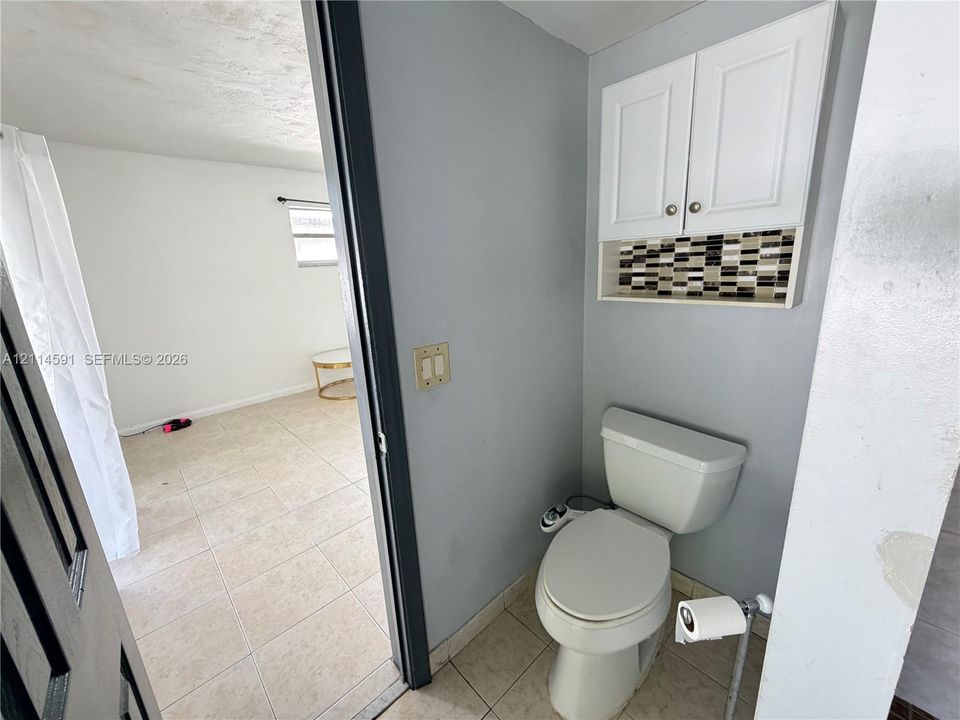 Wall-mounted white cabinetry featuring decorative tile backsplash, ceramic tile flooring, and a standard-height toilet
