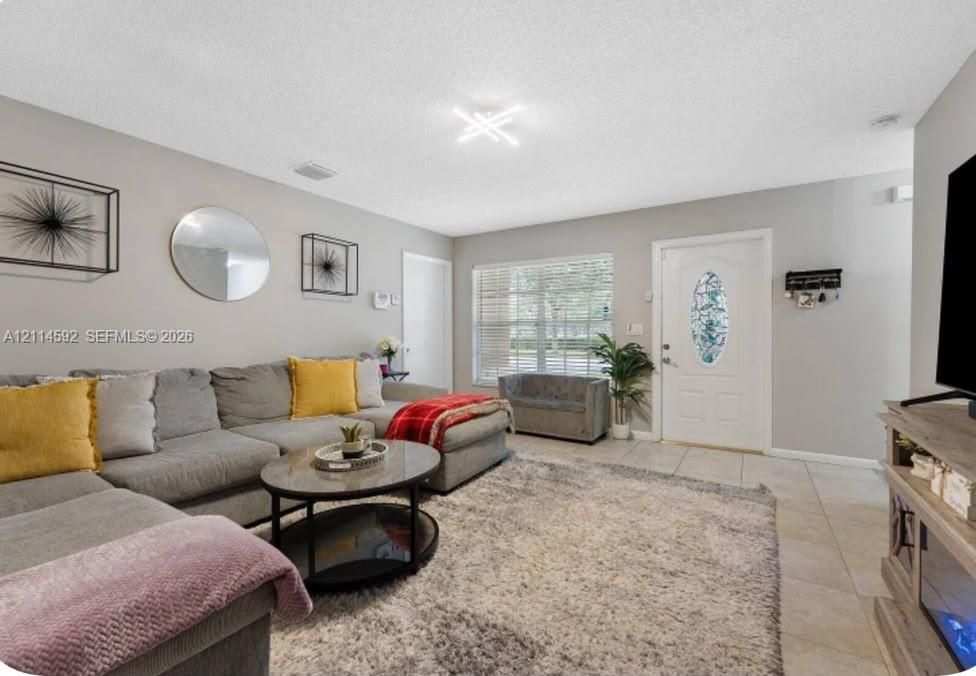 Neutral wall tones featuring tile flooring, multi-pane window, and decorative entry door with an oval glass insert, illuminated by a contemporary geometric light fixture