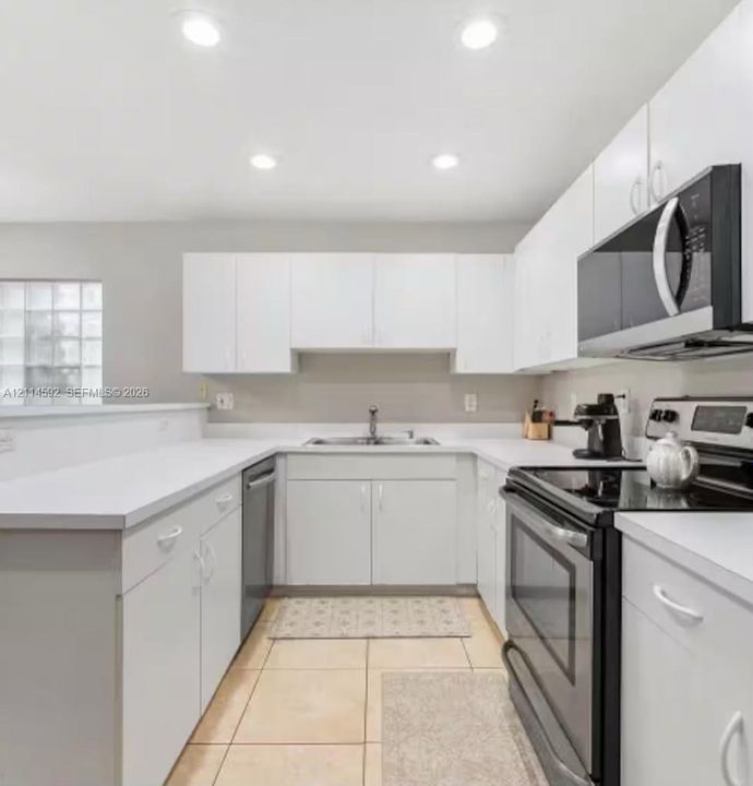 Kitchen featuring white cabinetry, solid-surface countertops, recessed ceiling lighting, a stainless steel over-the-range microwave, and ceramic tile flooring