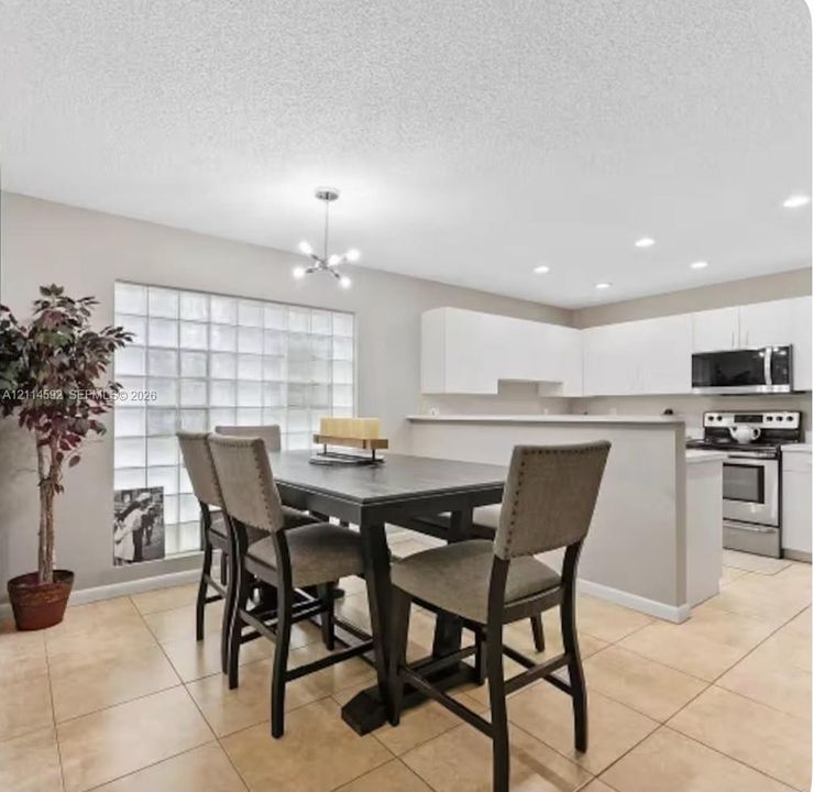 Kitchen featuring white cabinetry, stainless steel appliances, tile flooring, glass block window detailing, and recessed lighting