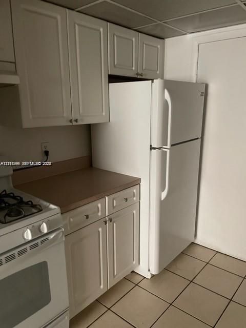 Kitchen featuring white shaker-style cabinetry, solid-surface countertops, square tile flooring, and a white top-mount refrigerator