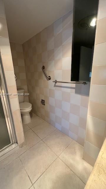 Bathroom featuring floor-to-ceiling checkerboard tile, large-format tile flooring, a glass-enclosed shower, and brushed metal hardware
