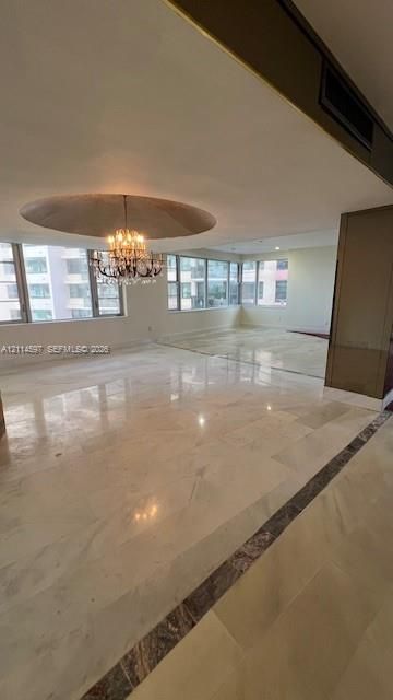 Polished stone flooring with decorative inlay, expansive floor-to-ceiling windows, recessed circular ceiling feature, and a crystal chandelier