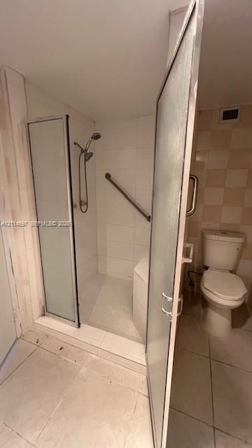 Walk-in shower enclosure featuring a handheld showerhead, integrated seating, and mounted grab bar, finished with white wall tiling and a standard toilet