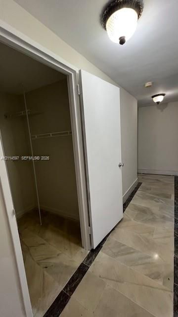 Hallway featuring stone tile flooring with decorative dark borders and flush-mount ceiling lighting, including a reach-in closet with built-in metal shelving