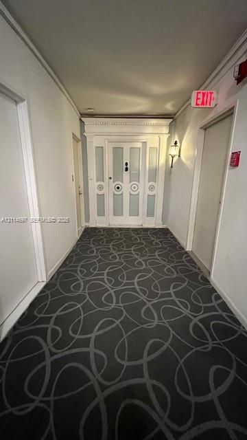 Hallway featuring patterned carpeting, paneled wood door with decorative molding, and wall-mounted sconce lighting
