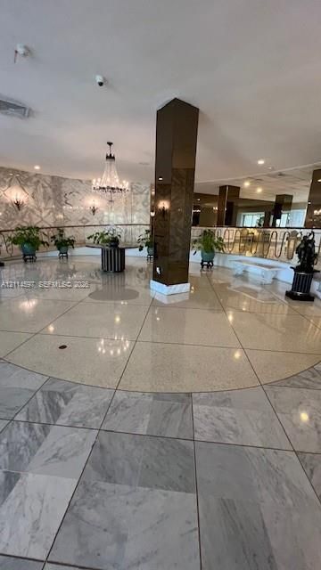 Grand foyer featuring polished stone flooring, custom-patterned wall finishes, a central structural column with a reflective finish, a multi-tiered crystal chandelier, and decorative metal railings