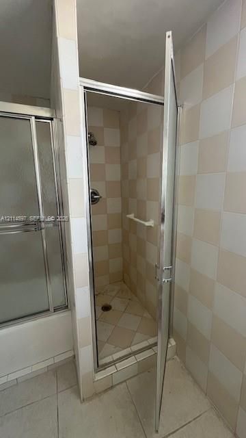 Walk-in shower enclosure featuring a chrome-framed hinged door, wall-mounted shower head, integrated towel bar, and checkerboard-patterned tile wall surfacing