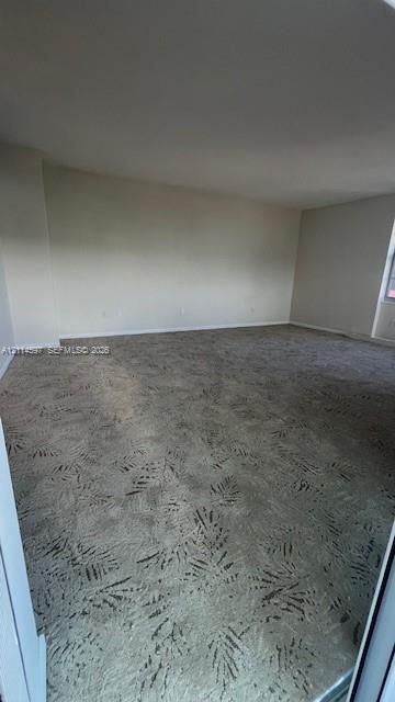 Spacious room featuring neutral wall paint and patterned carpeting
