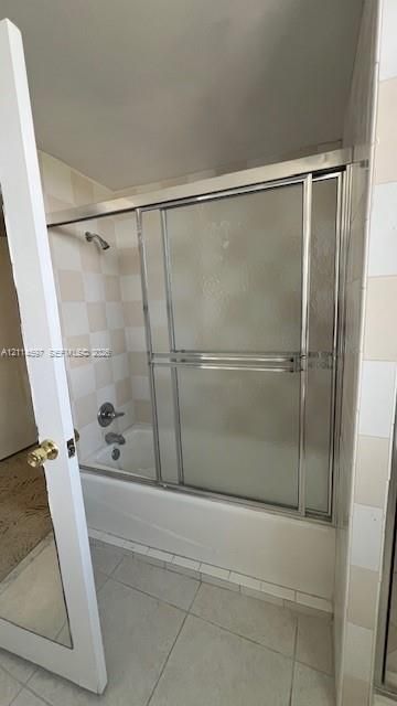 Tub and shower combination featuring a metal-framed glass sliding enclosure and a checkerboard pattern tile surround