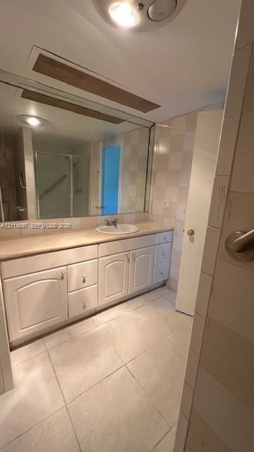 Bathroom featuring a large vanity with white cabinetry, integrated sink, and stone-surface countertop, complemented by floor-to-ceiling wall tiles and ceramic floor tiling