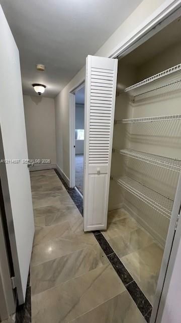 Storage closet with louvered bi-fold door, white wire shelving, and neutral tile flooring featuring dark stone-patterned accents