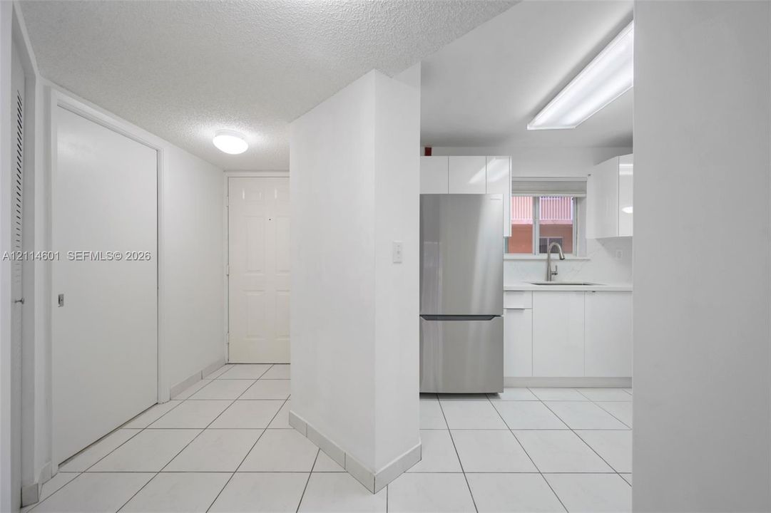 Kitchen featuring white cabinetry, stainless steel refrigerator, undermount sink, and white tile flooring