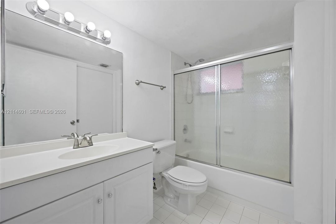 Bathroom featuring a white vanity with an integrated sink, full-width wall mirror, four-bulb vanity lighting fixture, and a tub-shower combination enclosed by textured glass sliding doors
