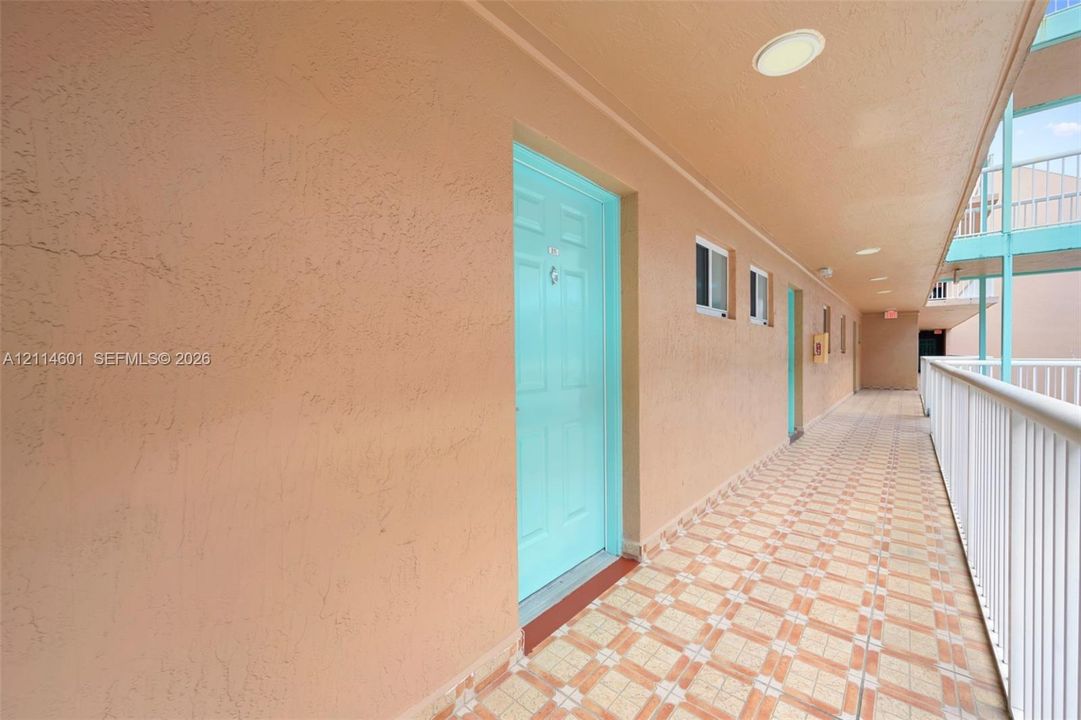 Exterior walkway featuring textured stucco walls, tiled flooring, recessed ceiling lighting, and white metal railing