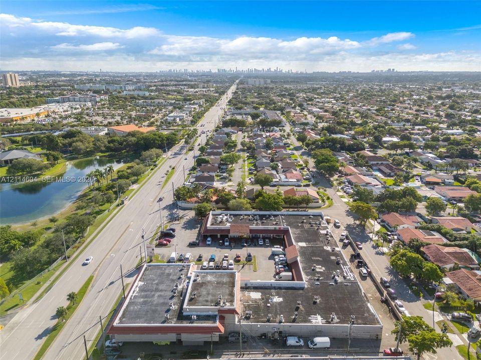 Aerial perspective of a multi-tenant commercial property featuring an L-shaped structure, expansive surface parking, and road frontage