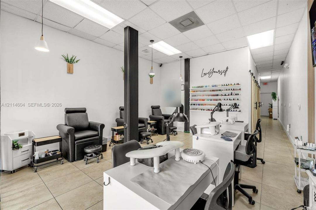 Commercial space featuring neutral ceramic tile flooring, built-in wall-mounted shelving, drop-ceiling grid lighting, and modern pendant fixtures