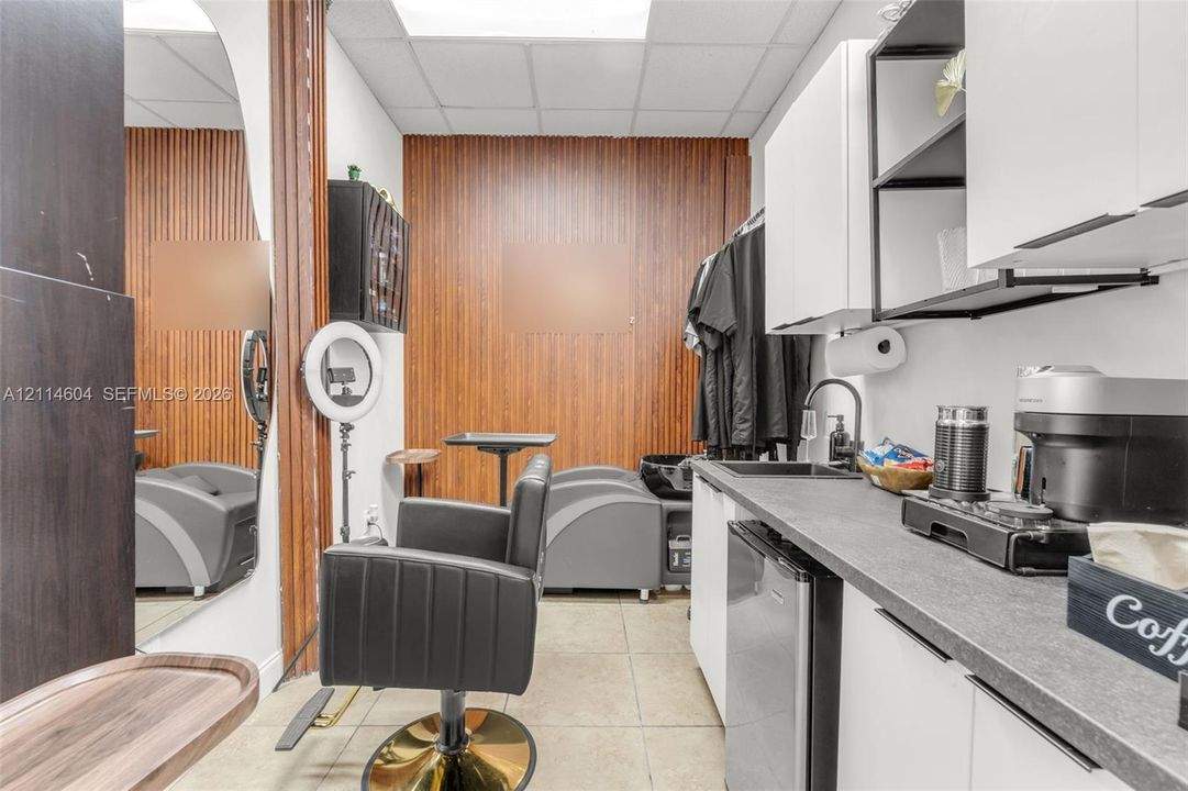 Custom workspace featuring vertical wood-slat wall paneling, tile flooring, and integrated kitchenette with a matte black faucet, dark countertop, and white cabinetry