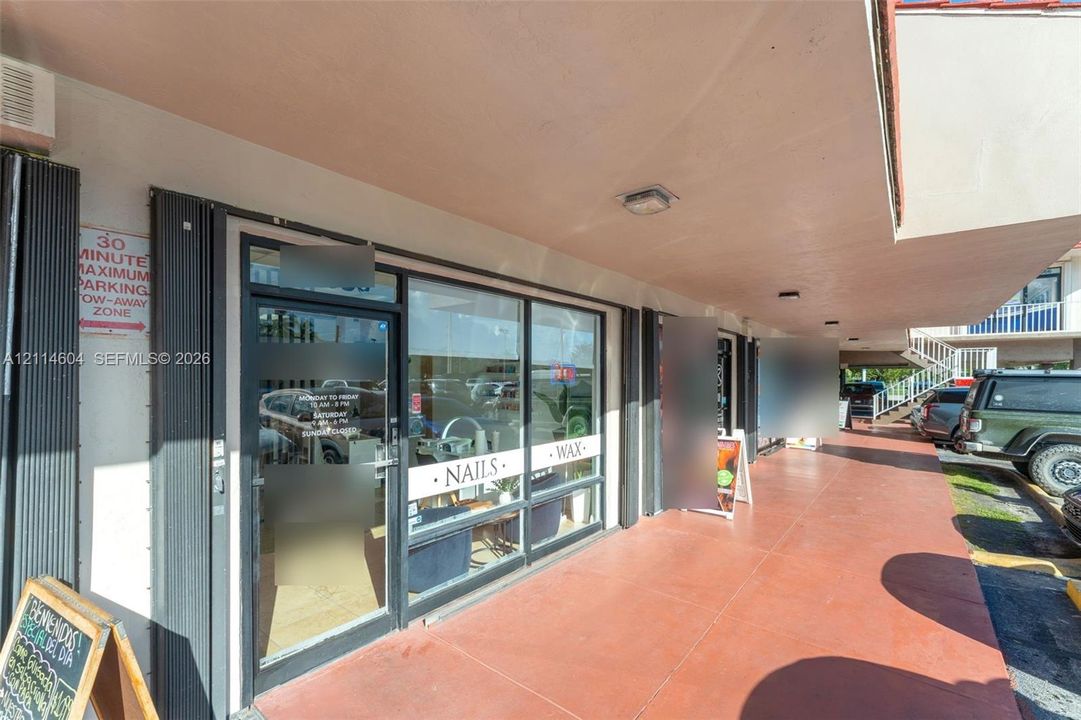 Commercial storefront featuring an expansive glass facade with aluminum framing, covered walkway with integrated exterior lighting, and terracotta-tone concrete flooring