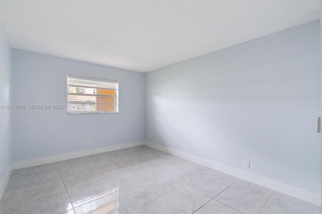 Neutral interior room featuring light-toned wall finishes, large-format tile flooring, and a horizontal louvered window