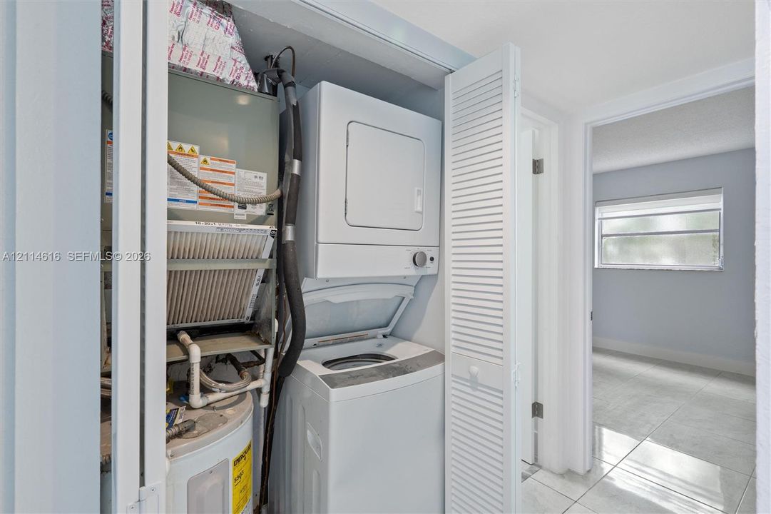 Utility closet featuring a stacked laundry appliance, water heater, HVAC air handler, and white louvered folding doors