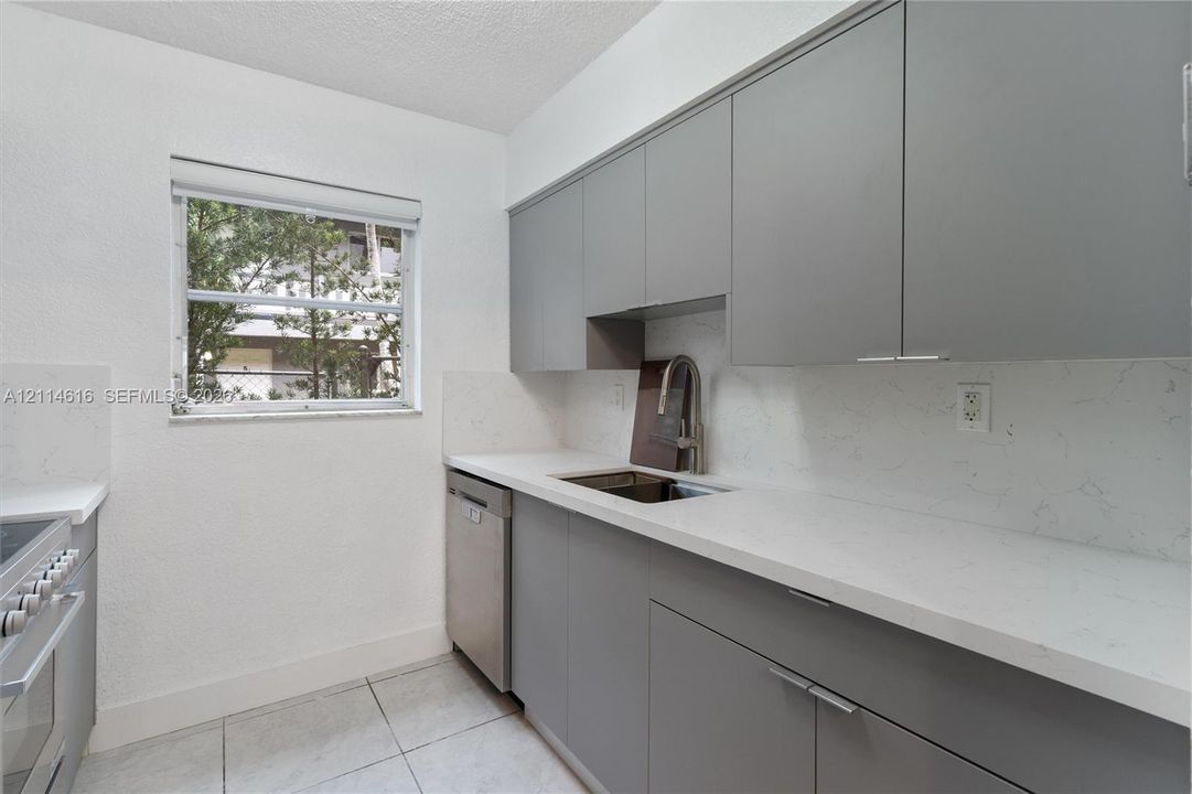 Kitchen featuring flat-panel gray cabinetry, solid-surface countertops with integrated backsplash, stainless steel dishwasher, and stainless steel pull-down faucet